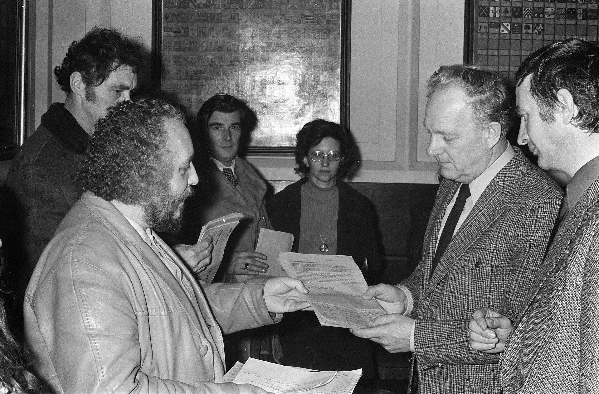 Buurtbewoners overhandigen een petitie aan twee wethouders tijdens een gemeenteraadsvergadering.